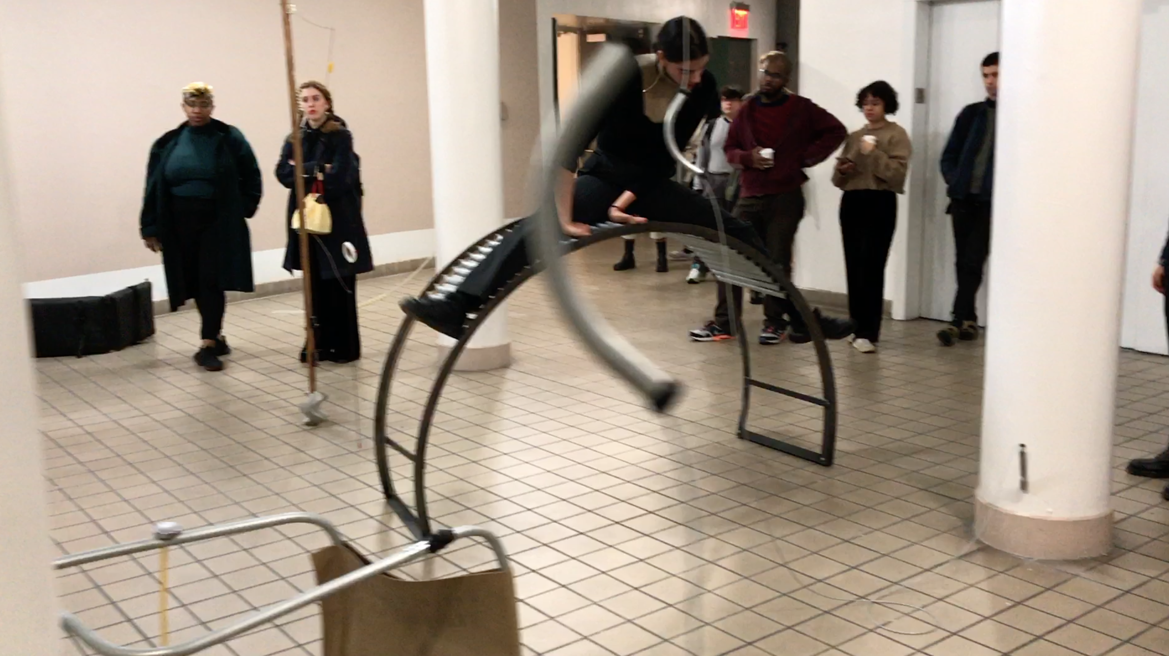 Performance still, body is interacting with a large curved metal instrument.