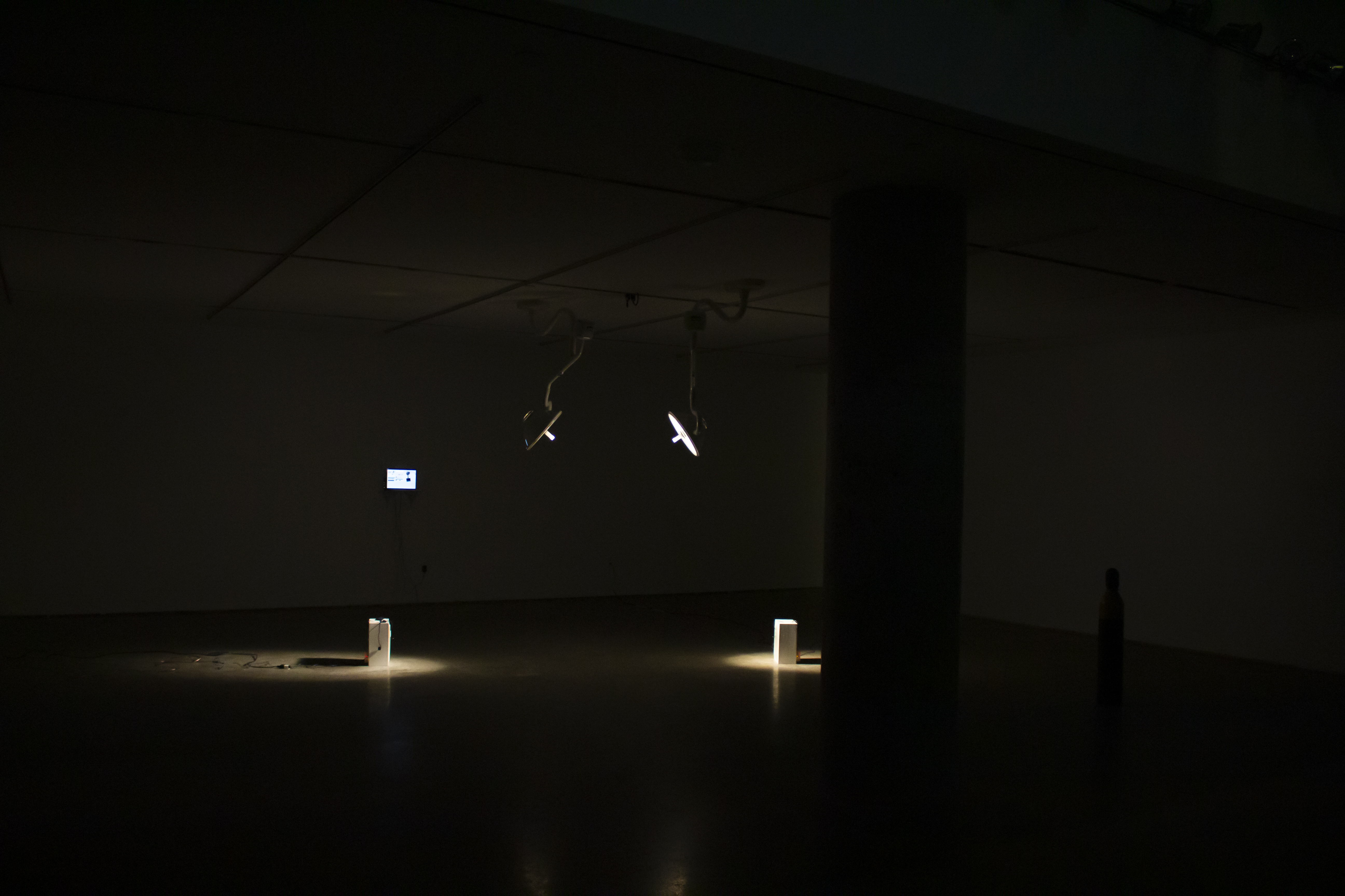 Installation view, two surgical lamps installed on the ceiling, each lighting two speakers accross the space.